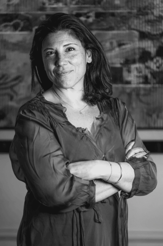 Portrait en noir et blanc D'Alexandra BERGHEIMER debout les bras croisés, devant un fond artistique dans son cabinet.